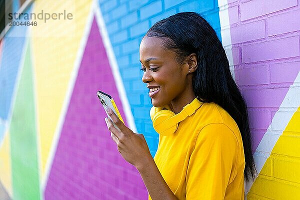 Afrikanische Frau  die lächelnd telefoniert und sich an eine bunte Wand in der Stadt lehnt