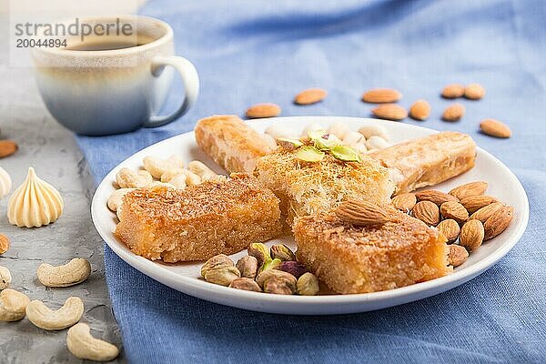 Traditionelle arabische Süßigkeiten (Basbus  Kunafa  Baklava)  eine Tasse Kaffee und Nüsse auf grauem Betonhintergrund und blauem Textil. Seitenansicht  Nahaufnahme  selektiver Fokus