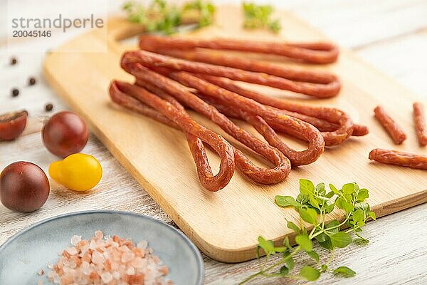 Traditionelle polnische geräucherte Schweinefleischwurst Kabanos auf Schneidebrett mit Salz und Pfeffer auf weißem Holzhintergrund. Seitenansicht  Nahaufnahme  selektiver Fokus