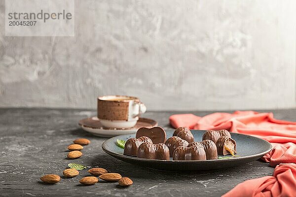 Schokoladenkaramellbonbons mit Mandeln und einer Tasse Kaffee auf einem schwarzen Betonhintergrund und rotem Textil. Seitenansicht  Kopierraum