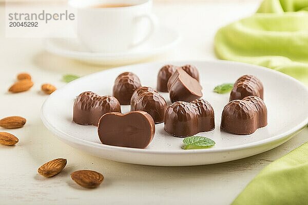 Schokoladenbonbons mit Mandeln und eine Tasse Kaffee auf weißem Holzhintergrund und grünem Stoff. Seitenansicht  Nahaufnahme  selektiver Fokus