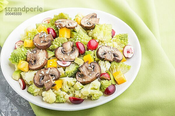 Vegetarischer Salat aus Romanesco Kohl  Champignons  Preiselbeeren  Avocado und Kürbis auf grauem Betonhintergrund und grünem Textil. Seitenansicht  Nahaufnahme  selektiver Fokus