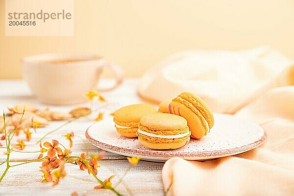 Orange Macarons oder Makronen Kuchen mit Tasse Aprikosensaft auf einem weißen hölzernen Hintergrund und orangefarbenen Leinen Textil. Seitenansicht  Nahaufnahme  selektiver Fokus