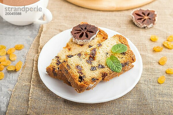 Hausgemachter Kuchen mit Rosinen  getrockneten Kaki und einer Tasse heißer Schokolade auf einem grauen Betonhintergrund und Leinenstoff. Seitenansicht  Nahaufnahme  selektiver Fokus