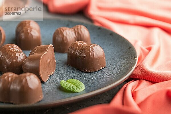 Schokoladenbonbons mit Mandeln und eine Tasse Kaffee auf einem schwarzen Betonhintergrund und rotem Textil. Seitenansicht  Nahaufnahme  selektiver Fokus