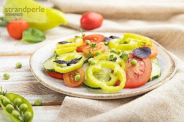 Vegetarischer Salat aus grünen Erbsen  Tomaten  Paprika und Basilikum auf weißem Holzhintergrund und Leinentuch. Seitenansicht  Nahaufnahme  selektiver Fokus