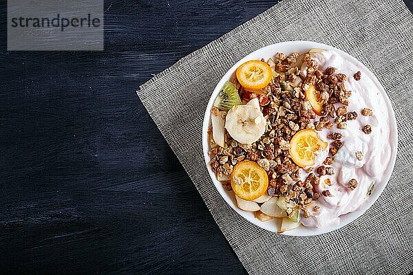 Vegetarischer Salat aus Bananen  Äpfeln  Birnen  Kumquats  Kiwi mit Granola und Joghurt auf schwarzem woodem Hintergrund  Draufsicht  Kopierraum