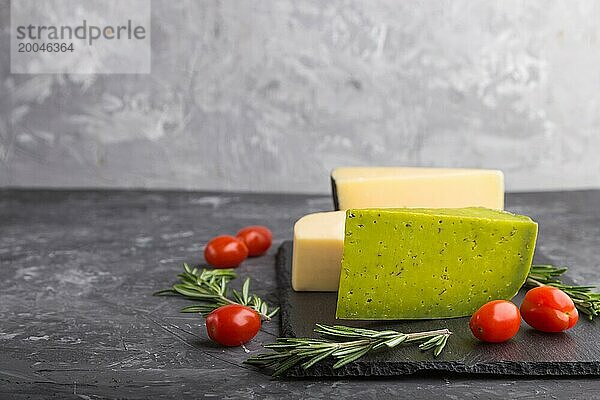 Grüner Basilikumkäse und verschiedene Käsesorten mit Rosmarin und Tomaten auf einer schwarzen Schiefertafel auf einem schwarzen Betonhintergrund. Seitenansicht  Nahaufnahme  Kopierraum  selektiver Fokus