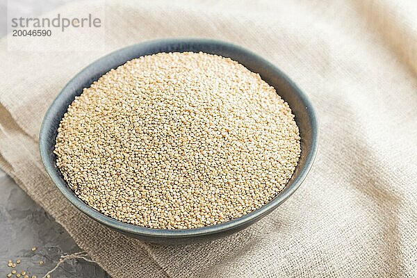 Blaue Keramikschale mit rohen weißen Quinoa Samen auf grauem Betonhintergrund und Leinenstoff. Seitenansicht  Nahaufnahme  selektiver Fokus