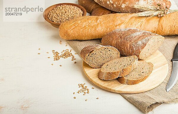 Aufgeschnittenes Brot mit verschiedenen Sorten frisch gebackenen Brotes auf weißem Holzhintergrund. Seitenansicht  Nahaufnahme  Kopierraum