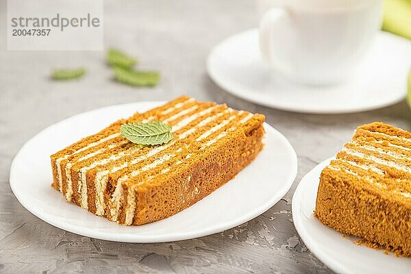 Hausgemachter Honigkuchen mit Milchcreme und Minze mit einer Tasse Kaffee auf einem grauen Betonhintergrund und grünem Textil. Seitenansicht  Nahaufnahme  selektiver Fokus