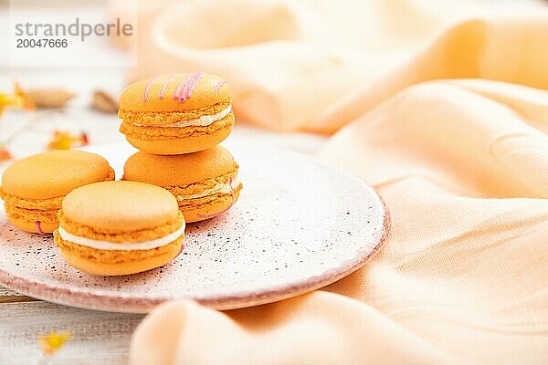 Orange Macarons oder Makronen Kuchen mit Tasse Aprikosensaft auf einem weißen hölzernen Hintergrund und orangefarbenen Leinen Textil. Seitenansicht  Nahaufnahme  selektiver Fokus