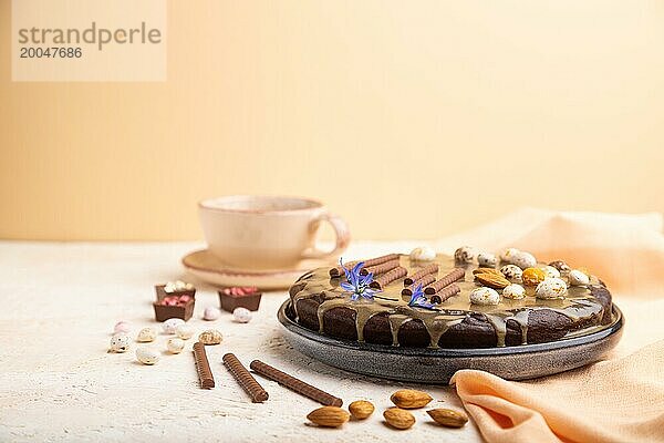 Hausgemachter Schokoladen Brownie Kuchen mit Karamellcreme und Mandeln mit einer Tasse Kaffee auf einem weißen und orangefarbenen Hintergrund und orangefarbenem Textil. Seitenansicht  Kopierraum  selektiver Fokus