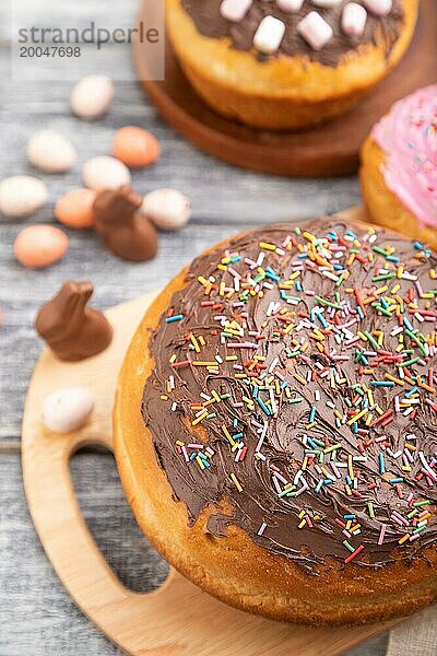 Hausgemachte glasierte und dekorierte Osterkuchen mit Schokoladeneiern und Kaninchen auf grauem Holzhintergrund und Leinentextil. Seitenansicht  selektiver Fokus  Nahaufnahme