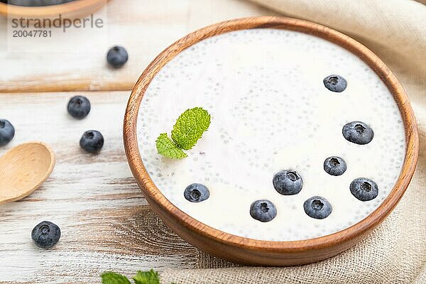 Joghurt mit Blaubeeren in einer Holzschale auf weißem Holzhintergrund und Leinenstoff. Seitenansicht  Nahaufnahme  selektiver Fokus