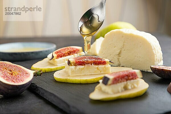 Sommerliche Vorspeise mit Birne  Hüttenkäse  Feigen und Honig auf Schieferplatte auf schwarzem Betonhintergrund. Seitenansicht  Nahaufnahme  selektiver Fokus