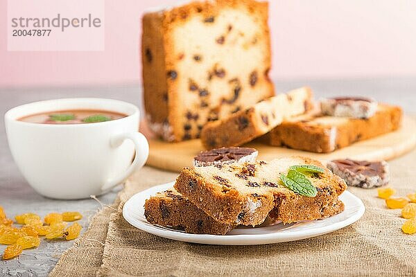 Hausgemachter Kuchen mit Rosinen  getrockneten Kaki und einer Tasse heißer Schokolade auf einem grauen Betonhintergrund und Leinenstoff. Seitenansicht  Nahaufnahme  selektiver Fokus