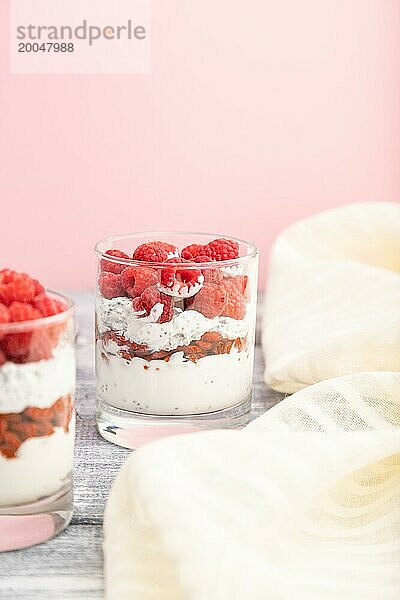 Joghurt mit Himbeeren  Goji Beeren und Chia Samen im Glas auf grauem und rosa Hintergrund und Leinenstoff. Seitenansicht  Kopierraum  selektiver Fokus