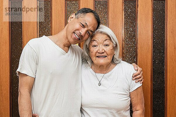 Glückliche ältere asiatische Mutter und erwachsener Sohn umarmen sich liebevoll  schauen in die Kamera  lächeln  genießen Familienbesuch  Freizeit