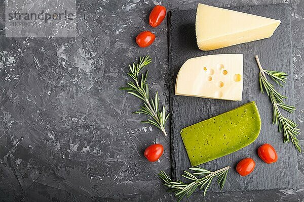 Grüner Basilikumkäse und verschiedene Käsesorten mit Rosmarin und Tomaten auf einer schwarzen Schiefertafel auf einem schwarzen Betonhintergrund. Seitenansicht  Nahaufnahme  Kopierraum  selektiver Fokus