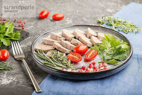 Gekochte Schweinezunge mit Tomaten und Kräutern auf einem schwarzen Betonhintergrund und blauem Leinentuch. Seitenansicht  Nahaufnahme  selektiver Fokus