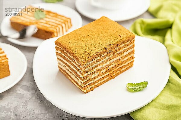 Hausgemachter Honigkuchen mit Milchcreme und Minze mit einer Tasse Kaffee auf einem grauen Betonhintergrund und grünem Textil. Seitenansicht  Nahaufnahme  selektiver Fokus