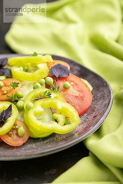 Vegetarischer Salat aus grünen Erbsen  Tomaten  Paprika und Basilikum auf einem schwarzen Betonhintergrund und grünem Textil. Seitenansicht  Nahaufnahme  selektiver Fokus