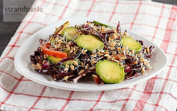 Vegetarischer Salat aus Purpurkohl  gekeimtem Weizen  Tomaten und Avocado auf Leinentischdecke  Nahaufnahme  selektiver Fokus  Seitenansicht