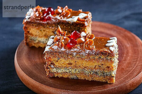 Ein Stück Kuchen mit Karamellcreme und Mohn auf einem hölzernen Küchenbrett. Nahaufnahme  selektiver Fokus  schwarzer Hintergrund