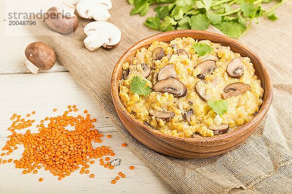 Linsenbrei mit Champignons und Koriander in einer Holzschale auf weißem Holzhintergrund und Leinentuch. Seitenansicht  Nahaufnahme  selektiver Fokus