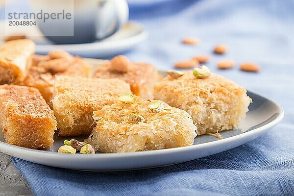 Traditionelle arabische Süßigkeiten (Basbus  Kunafa  Baklava) und eine Tasse Kaffee auf einem grauen Betonhintergrund und blauem Textil. Seitenansicht  Nahaufnahme  selektiver Fokus