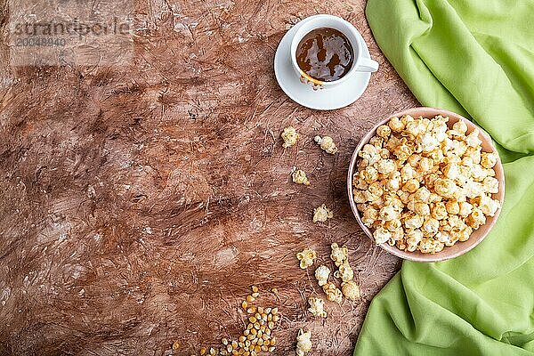 Popcorn mit Karamell in Keramikschale auf braunem Betonhintergrund und grünem Textil. Draufsicht  flat lay  copy space