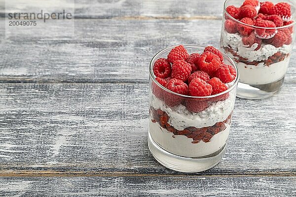 Joghurt mit Himbeeren  Goji Beeren und Chia Samen im Glas auf grauem Holzhintergrund. Seitenansicht  Nahaufnahme  selektiver Fokus  Kopierraum