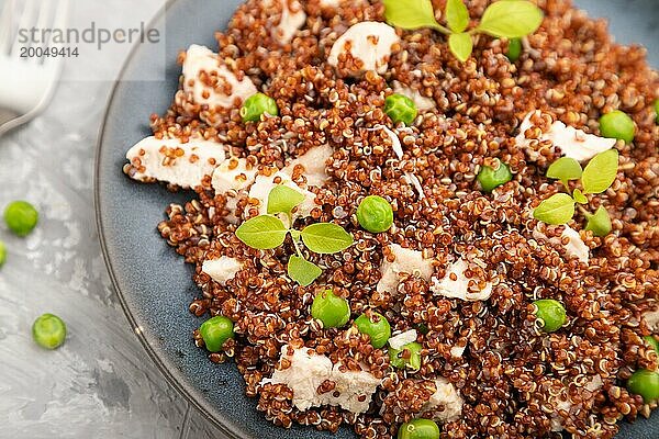 Quinoa Brei mit grüner Erbse und Huhn auf Keramikteller auf grauem Betonhintergrund und orangefarbenem Textil. Draufsicht  Nahaufnahme  selektiver Fokus