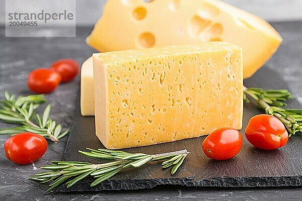 Verschiedene Käsesorten mit Rosmarin und Tomaten auf einer schwarzen Schiefertafel auf einem schwarzen Betonhintergrund. Seitenansicht  Nahaufnahme  selektiver Fokus