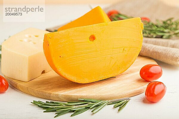 Verschiedene Käsesorten mit Rosmarin und Tomaten auf einem Holzbrett auf einem weißen Holzhintergrund und Leinenstoff. Seitenansicht  Nahaufnahme  selektiver Fokus