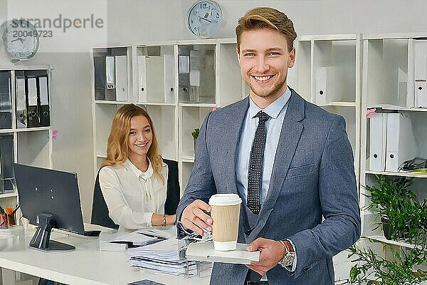 K generiert  Erfolgreicher Jungunternehmer sitzt zufrieden im Büro  30  35  Jahre  Mann  lächelt zufrieden  Existenzgründer  Firmenchef  bekommt einen Kaffee von seiner Büroangestellten