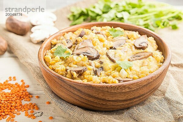 Linsenbrei mit Champignons und Koriander in einer Holzschale auf weißem Holzhintergrund und Leinentuch. Seitenansicht  Nahaufnahme  selektiver Fokus