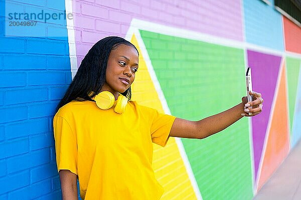 Seitenansicht Porträt einer jungen afrikanischen Frau posiert ein Selfie lehnt an einer bunten Wand