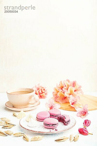 Lila Macarons oder Makronen Kuchen mit Tasse Kaffee auf einem weißen Beton Hintergrund mit Blumen verziert. Seitenansicht  Kopierraum  selektiver Fokus