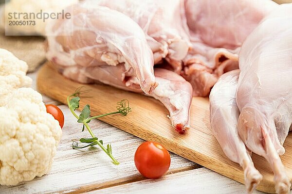 Ganzes rohes Kaninchen mit Blumenkohl  Tomaten und Gewürzen auf einem weißen Holzhintergrund und Leinenstoff. Seitenansicht  Nahaufnahme  selektiver Fokus