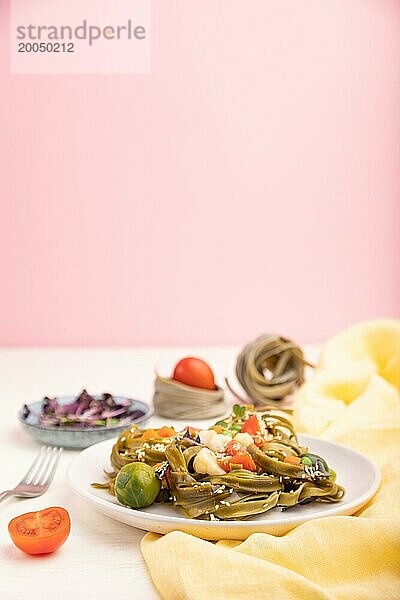 Tagliatelle mit grünem Spinat  Tomaten  Erbsen und Sprossen auf weißem und rosa Hintergrund und gelbem Stoff. Seitenansicht  Kopierraum  selektiver Fokus