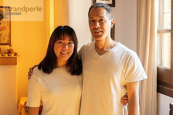 Erwachsene Geschwister japanischer Abstammung  die sich umarmen  lächeln und in die Kamera schauen. Horizontales Porträt in Innenräumen mit warmem Licht