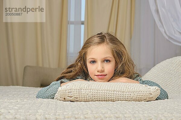 Junges Mädchen genießt einen Moment der Entspannung  liegend Gesicht nach unten auf einem bequemen Bett mit weichen Kissen in einem gemütlichen Schlafzimmer. Die weichen Texturen und die warme Beleuchtung schaffen eine friedliche und heitere Atmosphäre  perfekt für Ruhe und Entspannung