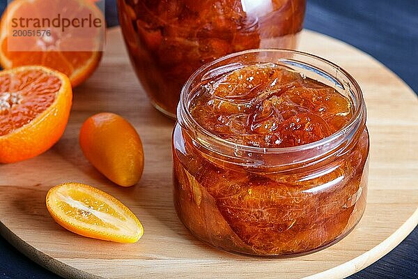 Mandarinen und Kumquatmarmelade in einem Glas mit frischen Früchten auf einem schwarzen Holztisch. Hausgemacht  Nahaufnahme