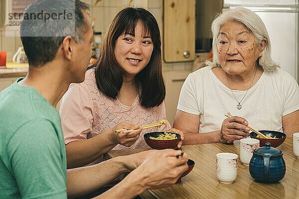 Ältere japanische Mutter mit erwachsenen Kindern beim Mittagessen zu Hause. Konzept von Familie  Tradition und ethnischer Vielfalt