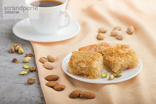 Traditionelle arabische Süßigkeiten (basbus  kunafa  baklava) und eine Tasse Kaffee auf einem grauen Betonhintergrund und orangefarbenem Textil