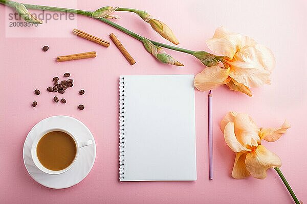 Orange Irisblüten und eine Tasse Kaffee mit Notizbuch auf pastellrosa Hintergrund. Morninig  Frühling  Mode Zusammensetzung. Flachlage  Draufsicht  Kopierraum