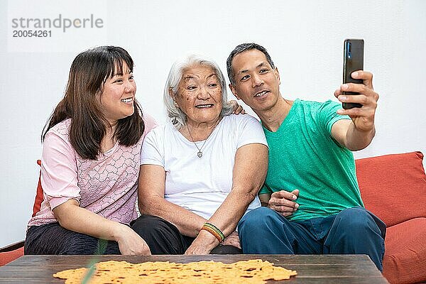 Erwachsene Kinder und ältere weißhaarige Mutter  ethnische japanische Familie  machen ein Selfie auf einem Sofa sitzend und lächelnd und teilen einen Familienmoment