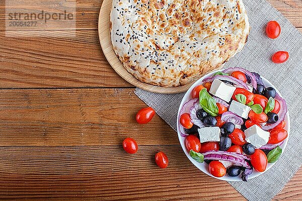 Griechischer Salat mit frischen Kirschtomaten  Fetakäse  schwarzen Oliven  Basilikum und Zwiebeln auf Holzuntergrund  Pfannkuchen  Draufsicht  Kopierraum
